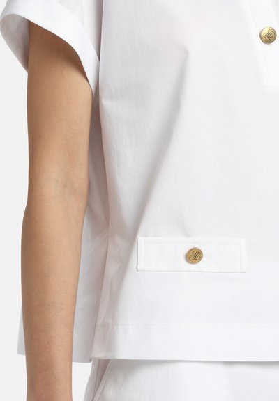 Fehér, rövid ujjú felső könnyű anyagból. Varrt zsebbel, arany gomb részlettel, és laza szabással.