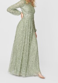 Lång, svävande klänning i ljusgrön tyg, prydd med spridda silverpaljetter. Har långa ärmar och en figursydd midja.