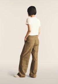 Pantalons larges vert olive avec des motifs découpés. Accompagnés d'un t-shirt blanc à manches courtes. Style décontracté, avec des poches latérales.