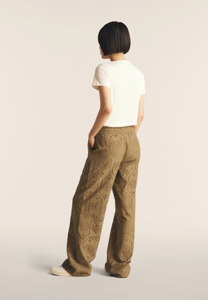 Pantaloni a gamba larga verde oliva con motivi a intaglio. Abbinati a una t-shirt bianca a maniche corte. Stile casual, con tasche laterali.