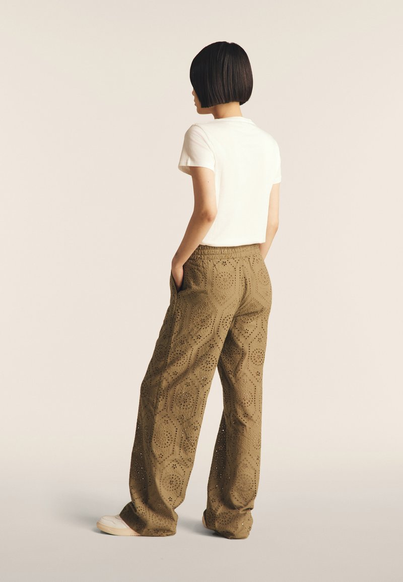 Pantalons larges vert olive avec des motifs découpés. Accompagnés d'un t-shirt blanc à manches courtes. Style décontracté, avec des poches latérales.