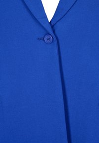 Blå kavaj med en slät, enhetlig textur, snedskuren krage och en enda blå knapp med fyra hål för fastsättning.