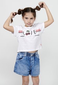 Baltas trumpas T-shirt su "MEILĖ" ir vyšnių grafika, derinamas su mėlynomis džinsinėmis šortais, turinčiais surinktą juosmenį ir kišenes.
