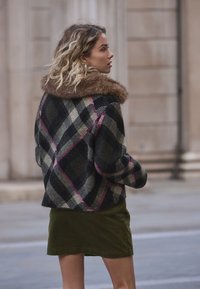 Karierte Wolljacke in Marineblau, Grün und Pink mit braunem Pelzkragen; kombiniert mit einem olivgrünen Cordrock.