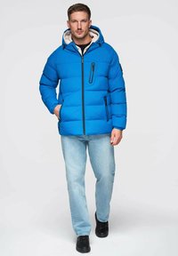 Sininen toppatakki vetoketjulla edessä, hupulla ja kahdella sivutaskulla. Sisäpuoli beigen värinen ja vaakasuunnassa tikattu. Yhdistetty vaaleiden farkkujen kanssa.