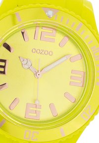 Montre en silicone jaune vif avec un cadran rond, des index et des aiguilles en or rose. Comprend une échelle des minutes et le logo de la marque.