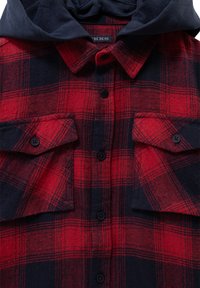 Rood en marineblauw geruite flanellen shirt met knopen, twee borstzakken en een capuchon. De gestructureerde stof toont een gedurfde geruite print.