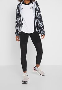 Černo-bílé vzorované větrovky, bílé sportovní tričko s černými akcenty, černé legíny a vícebarevné běžecké boty.