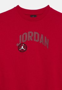 Κόκκινο t-shirt με στρογγυλή λαιμόκοψη και το κείμενο "JORDAN" καθώς και λογότυπο μπάσκετ που απεικονίζει τον αριθμό 23 και μια φιγούρα που πηδάει σε λευκό και μαύρο.