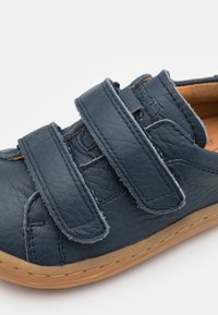 Zapato de cuero azul con dos correas ajustables de velcro, detalles de costura y una suela de goma. El interior presenta un forro beige.