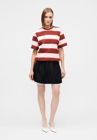 Κοντομάνικο πουκάμισο με κόκκινες και ροζ ρίγες συνδυασμένο με μαύρη φούστα που διαθέτει κεντήματα με λουλούδια, φορεμένα με καλσόν με δαντέλα και λευκά τακούνια.