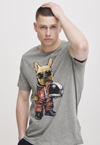 Grå bomulls T-skjorte med et tegneseriehund med solbriller, iført en oransje romdrakt og holder en svart hjelm. Korte ermer, casual passform.