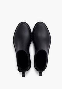 Botas de tobillo de goma negra con una textura suave, paneles laterales elásticos y tiradores para ponerlas fácilmente. Punta redondeada y diseño minimalista.