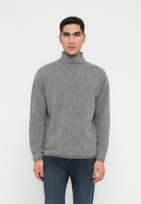 Pullover de gola alta cinza em tecido macio, com um ajuste descontraído e punhos canelados. Combinado com jeans de denim escuro.