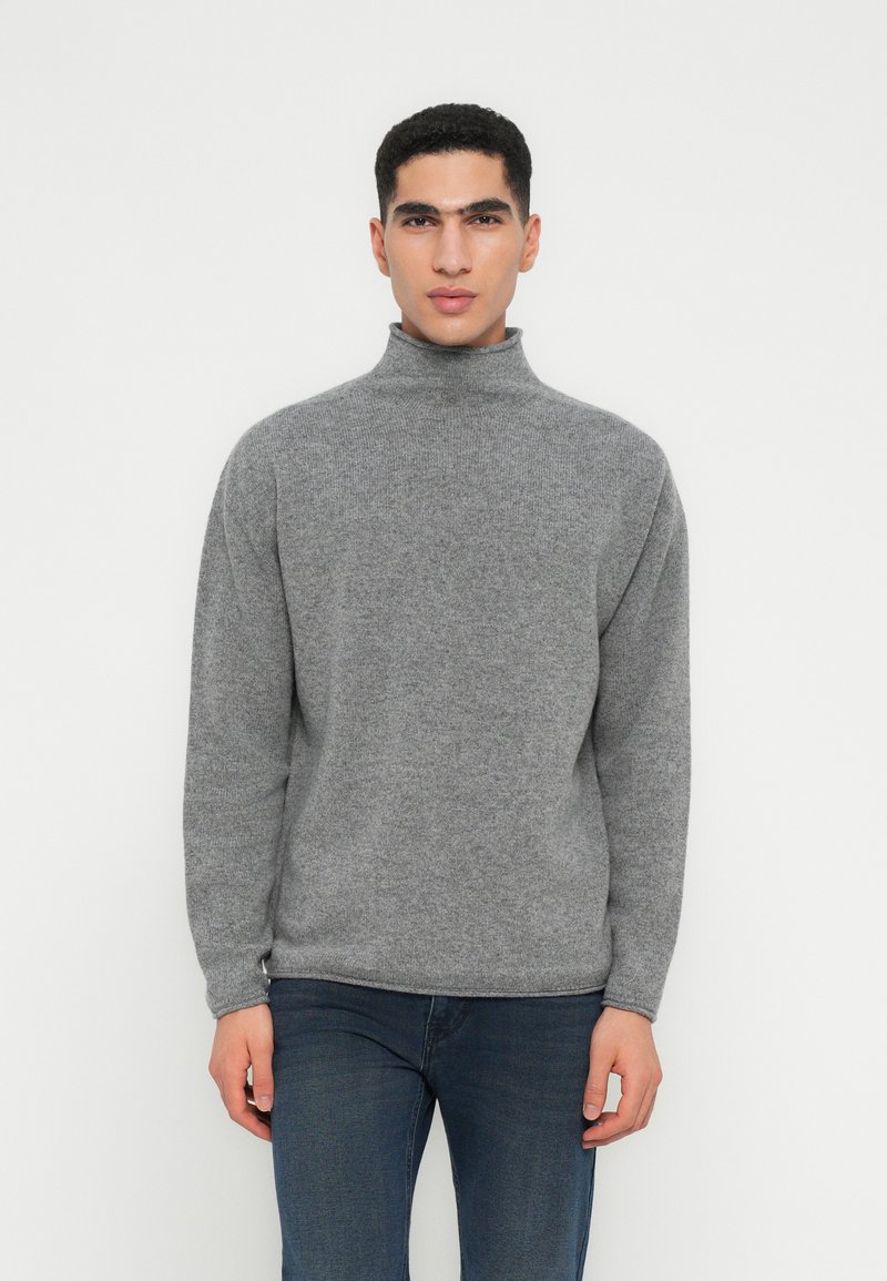 Pullover de gola alta cinza em tecido macio, com um ajuste descontraído e punhos canelados. Combinado com jeans de denim escuro.