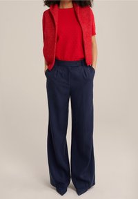 Röd stickad kortärmad topp med textur, tillsammans med marinblå vida byxor med framknapp och sidofickor.