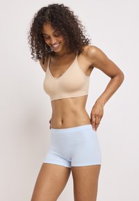 Beige sömlös bralette med justerbara remmar och ljusblå mjuka boyshorts. Båda har en slät textur och sitter tätt mot huden.