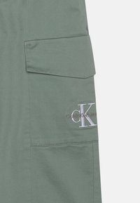 Zelene cargo kratke hlače s prednjim džepom, CK logotipom vezom u srebrnoj boji i urednim detaljima šivanja. Izrađene su od tkanine.