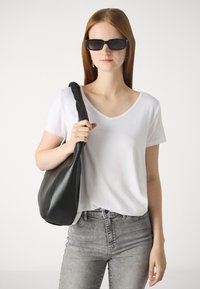 Bela kratka majica s V-izrezom, sivi uski traperice, velika crna kožna torba preko ramena, model nosi tamne sunčane naočale, glatke površine.