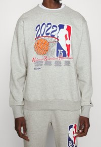 Sweat-shirt gris avec un grand graphisme représentant un panier de basket, un ballon orange et le logo NBA. Poignets et ourlet côtelés, coupe décontractée.