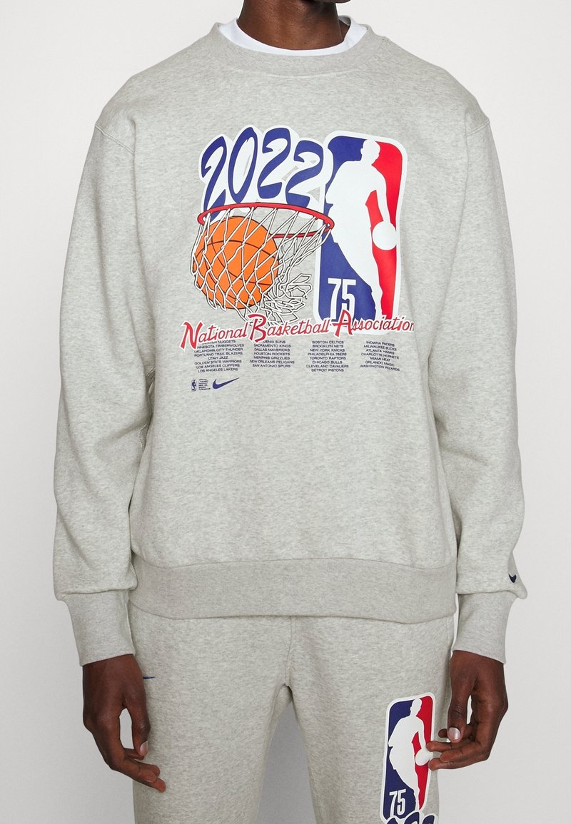 Sweat-shirt gris avec un grand graphisme représentant un panier de basket, un ballon orange et le logo NBA. Poignets et ourlet côtelés, coupe décontractée.