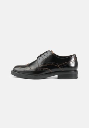 Black leather dress shoe with brogue detailing, sleek rounded shape, black sole, and contrasting orange stitching along seams.
