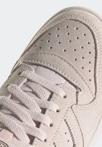 Light pink suede sneaker with perforated toe box, flat laces, and textured side panels. Features white midsole and stitching accents.