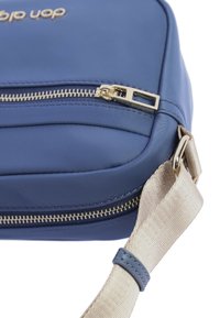 Bolso bandolera de nylon azul con superficie texturizada, cremallera dorada y correa ajustable de color crema. Presenta un compartimento con cremallera prominente.