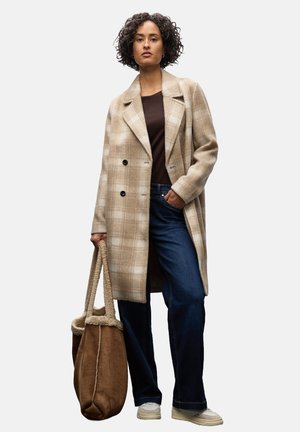 Beige kariertes Coat mit zwei schwarzen Knöpfen, braunem Oberteil, dunkelblauen Jeans und einer braunen Taschen mit Schaffellfutter. Tanfarbene Sneakers runden den Look ab.