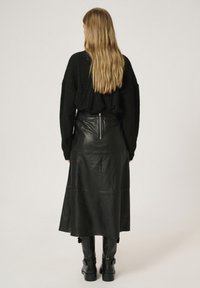 Sort strikket sweater med oversized pasform, parret med en højtaljet, knælang sort lædernederdel med lynlåsdetalje bagpå.