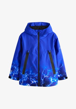 Blauwe jas binnenkant met bliksemschichtpatroon en zwart label dat waterdicht, winddicht en gesealde naden beschrijft, opengehouden door een hand.