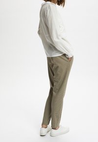 Vit bomullsblus med puffärmar och spetsdetaljer, ihop med beige rutiga byxor och vita sneakers, sedd från sidan.