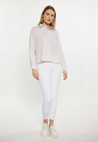 Camicia a righe in rosa pallido e bianco, con colletto e maniche lunghe, abbinata a jeans skinny bianchi e sneakers bianche.