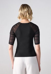 Top negru ajustat cu mâneci puff transparente, material texturat pe umeri și corp neted. Mâneci scurte și un decolteu rotund completează designul.