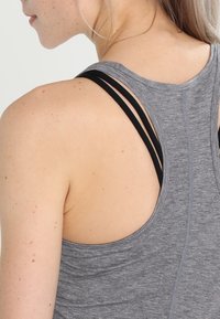Graues Sporttop mit Racerback-Design. Es verfügt über dünne schwarze Träger und einen weichen, strukturierten Stoff. Die Rückseite ist freigelegt mit sichtbaren Nähten.