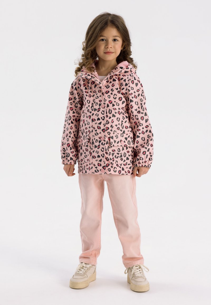 Rosa leopardmönstrad regnjacka med huva, långa ärmar och framficka; kombinerad med ljusrosa byxor och krämfärgade sneakers.