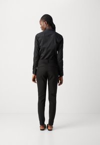 Maglietta nera a maniche lunghe e pantaloni neri, realizzati in tessuto morbido, silhouette aderente, con colletto e dettagli delle tasche posteriori.