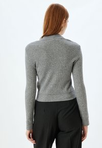 Maglione grigio a coste con design aderente, maniche lunghe e lunghezza crop. Presenta un tessuto strutturato e un collo semplice.