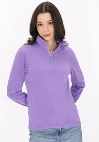 Pullover in pile viola con collo a mezza zip, texture morbida, maniche lunghe e silhouette leggermente aderente. Indossato con jeans blu.