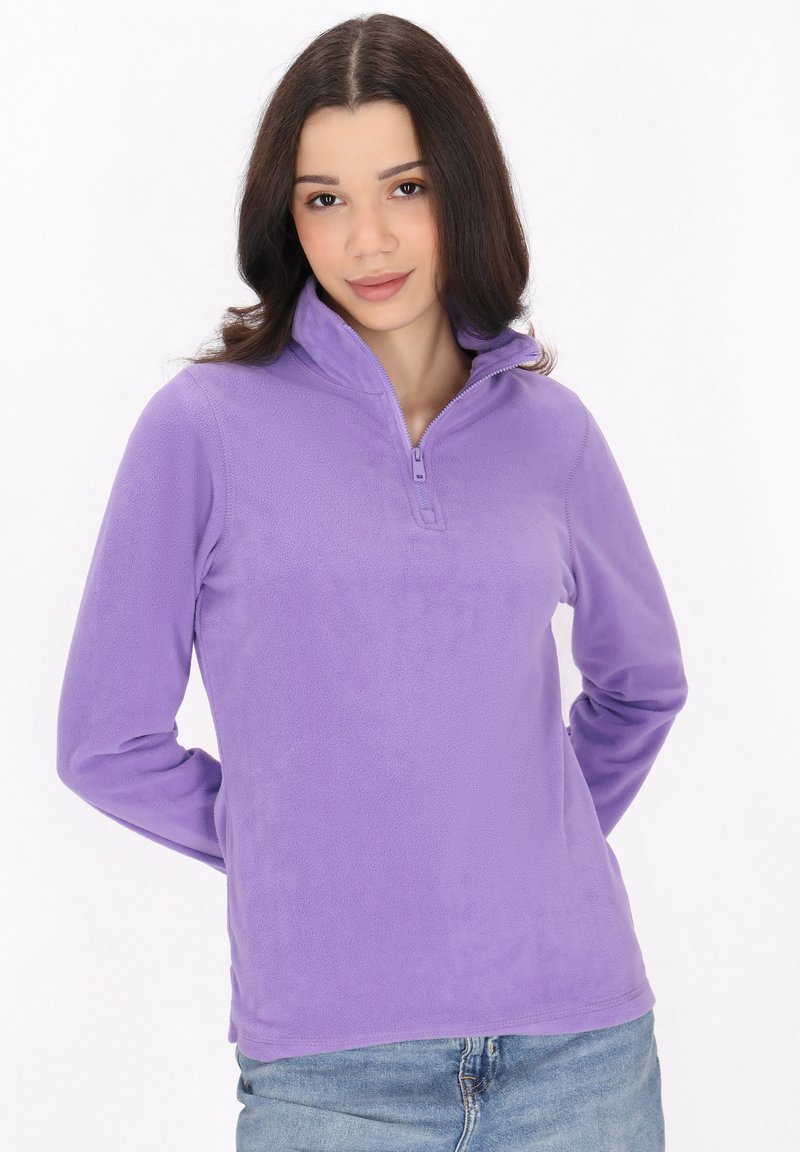 Pullover in pile viola con collo a mezza zip, texture morbida, maniche lunghe e silhouette leggermente aderente. Indossato con jeans blu.