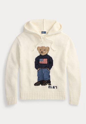 Krémová mikina z pletenej látky s dizajnom plyšového medvedíka oblečeného v svetri s americkou vlajkou a modrých džínsoch. Lemované manžety a spodný lem.