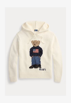 Sudadera con capucha de color crema hecha de tela de punto, con un diseño de oso de peluche que lleva un suéter con la bandera estadounidense y pantalones vaqueros azules. Puños y dobladillo acanalados.