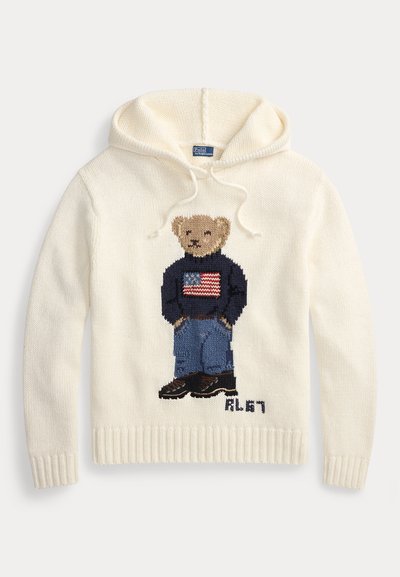 Φούτερ σε κρεμ απόχρωση από πλεκτό ύφασμα, με σχεδίαση αρκουδάκι που φοράει πουλόβερ με την αμερικανική σημαία και μπλε τζιν. Ριμπ μανσέτες και τελείωμα.