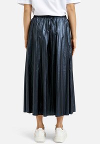 Navy pleated midi skirt made of shiny fabric with an elastic waistband, trimmed at the hem, worn with white sneakers.