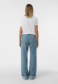 Jeansy z szerokimi nogawkami z jasnego denimu z postrzępionymi brzegami, połączone z białym t-shirtem z okrągłym dekoltem. Widoczne tylne kieszenie i minimalne detale szwów.