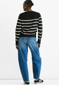 Black and white striped sweater with a round neck, paired with loose blue denim jeans and black sneakers; rear view highlighting the stripes.