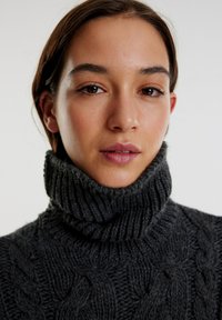 Fleischiger grauer Kabelstrickpullover mit hohem geripptem Rollkragen. Verfügt über eine dicke Textur und ein tailliertes Design, das Wärme und Komfort betont.