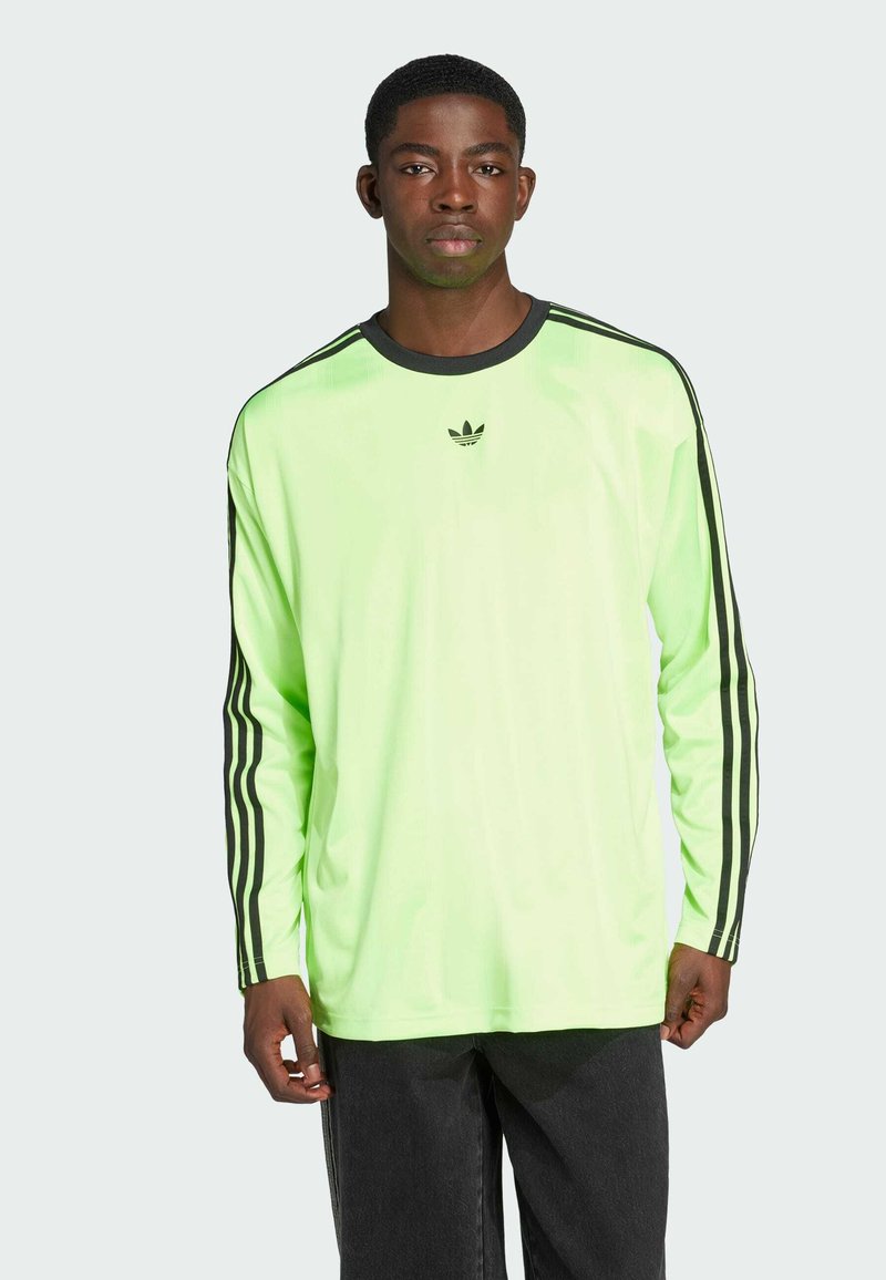 Neon zaļš garām piedurknēm krekls ar melniem akcentiem, ar trim melnām svītrām uz piedurknēm un mazu melnu logotipu uz krūtīm.