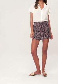 Valkoinen lyhythihainen napitettava paita, joka on yhdistetty tummansiniseen kukkakuvioiseen hameeseen, jossa on pieniä punaisia ja valkoisia kukkia. Vaaleat liukuhihnasandaalit.