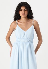 Ανοιχτό μπλε αμάνικο φόρεμα με V-λαιμόκοψη, ελαστική μέση και ροή στο κάτω μέρος. Λείος ύφασμα με απαλό ένδυμα.